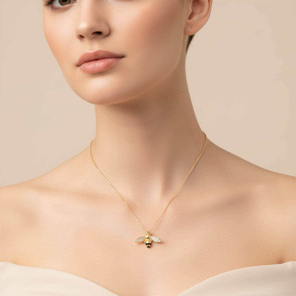 Gold bee pendant necklace on a white background around the neck of an attractive model.