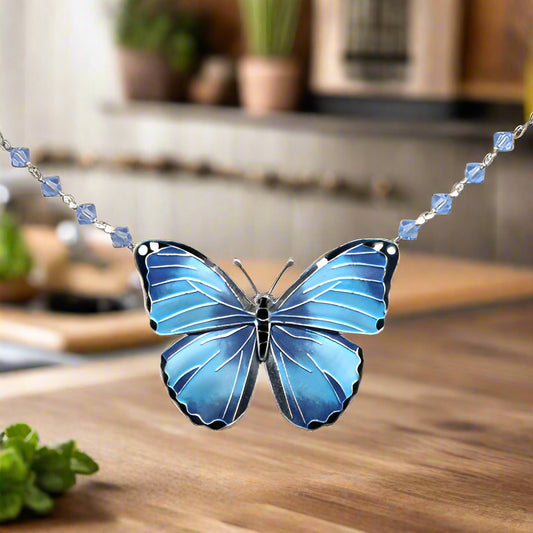 A blue butterfly pendant necklace with embellishments on a sterling silver chain.