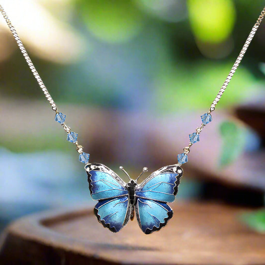 A sterling silver necklace featuring a cloisonne enamel blue morpho butterfly pendant with a sterling silver chain and Swarovski crystals.